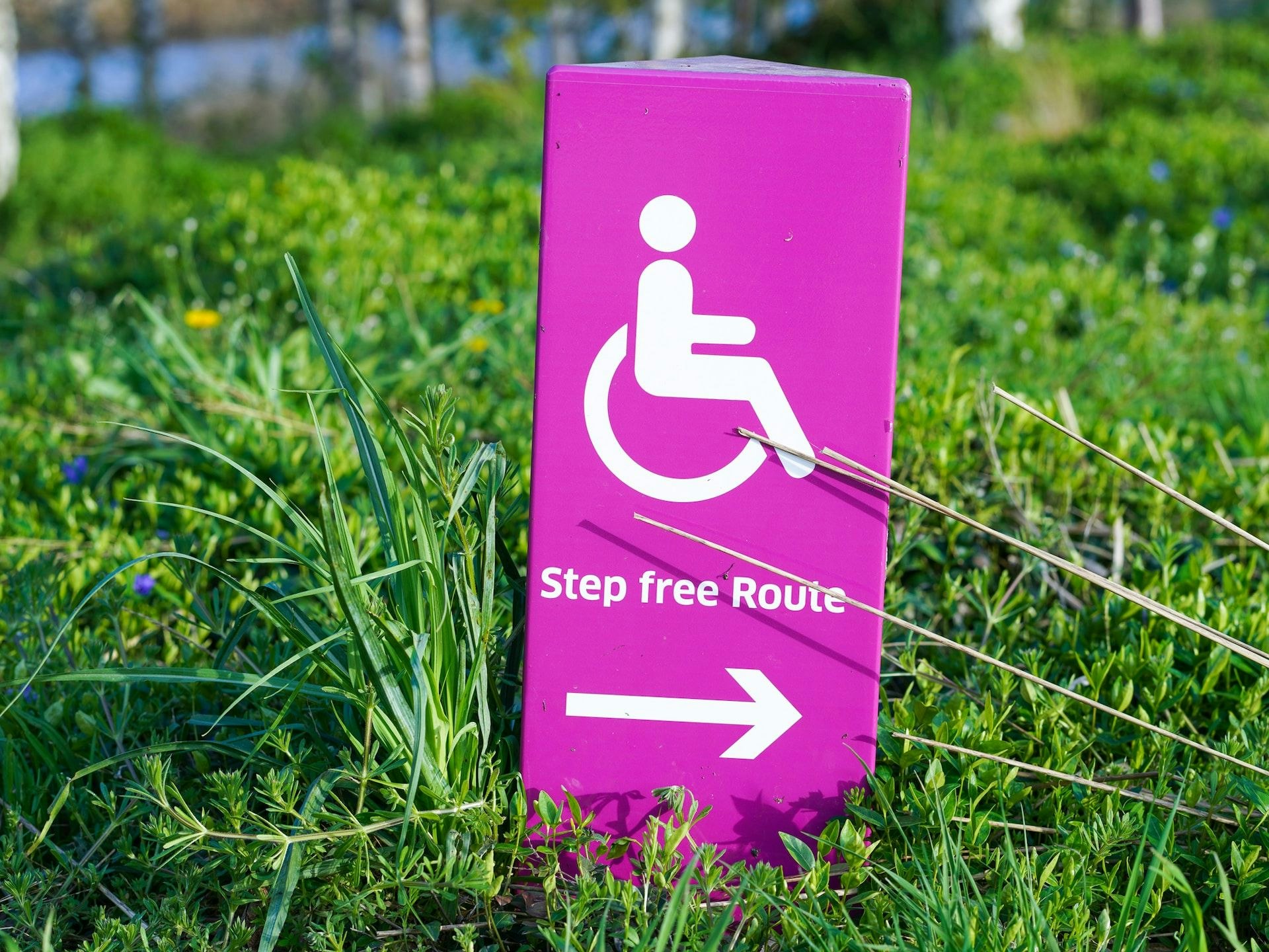 pink sign in the grass with icon of wheelchair user and an arrow, reading step-free route