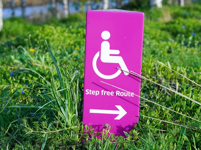 pink sign in the grass with icon of wheelchair user and an arrow, reading step-free route