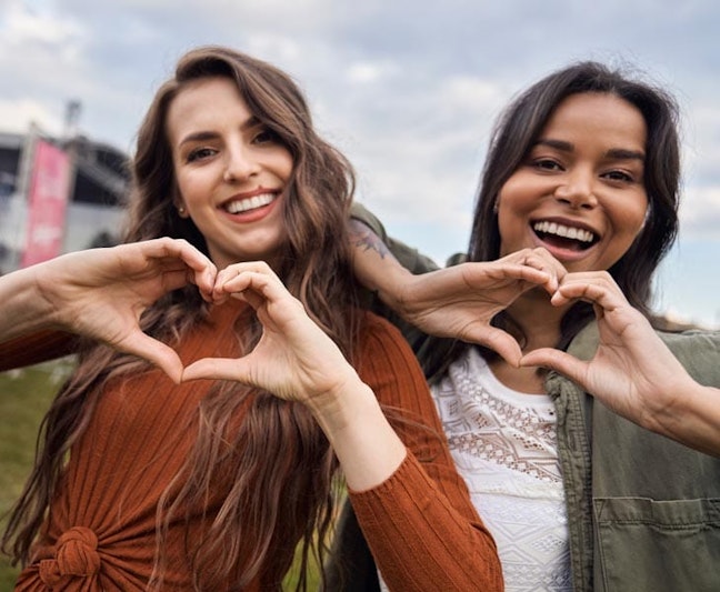 Two women striking the #InspireInclusion pose (Heart sign with hands)