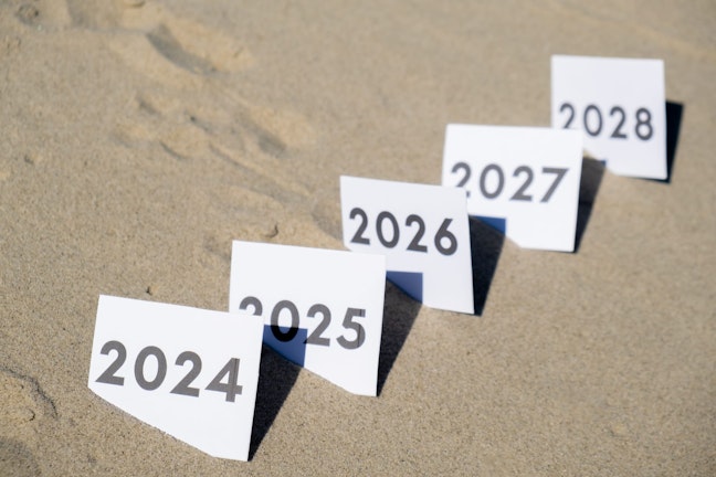 Paper in sand with years from 2024-2028 on